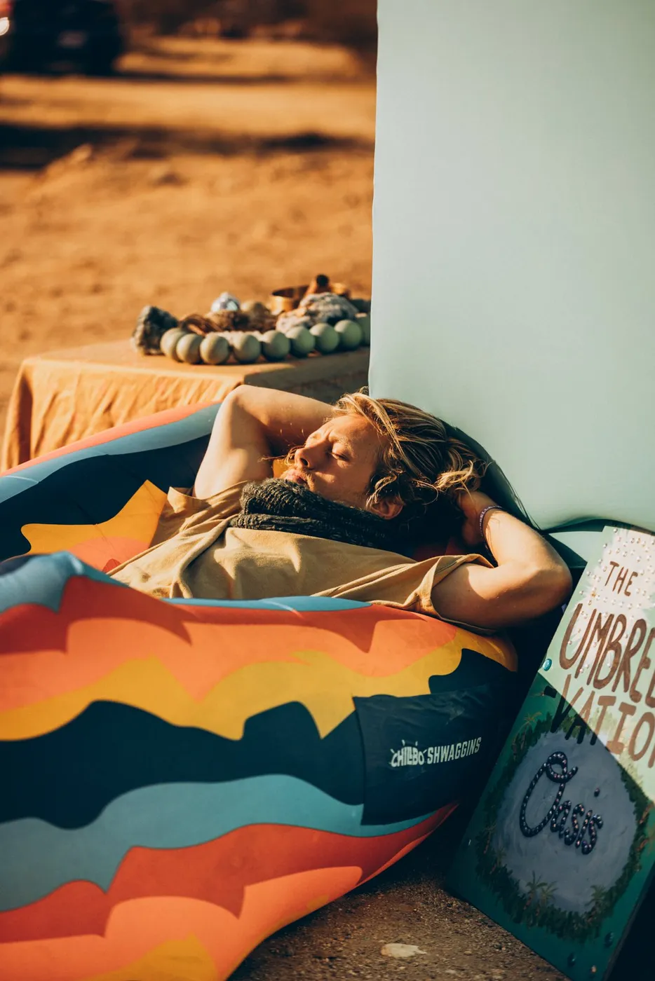 Someone napping on a sunset-print beanbag beside the hand-painted Umbrellavation Oasis sign